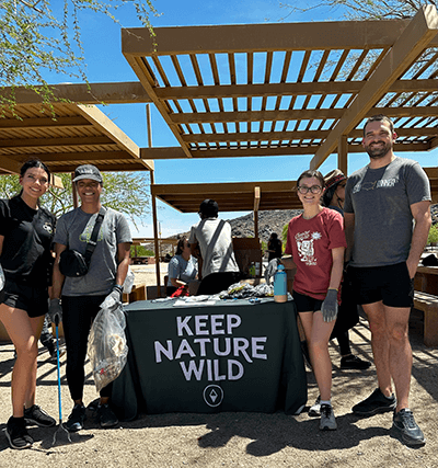Four Proctorio coworkers standing around a 'Keep Nature Wild' table under the sunny desert sky