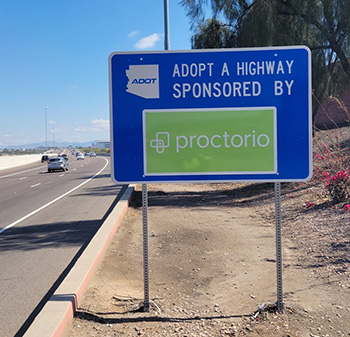 A sunny highway with an Adopt-A-Highway sign sponsored by Proctorio