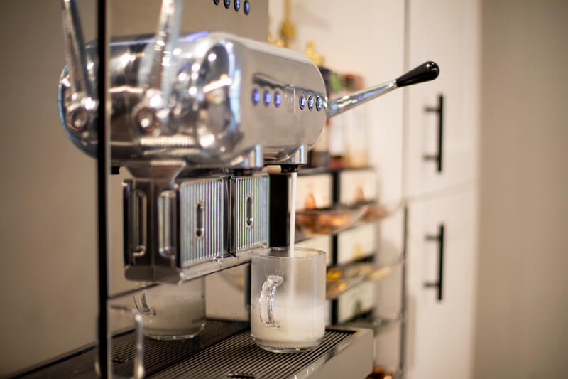 A high-end Nespresso machine pours warm milk into a beverage in a mug